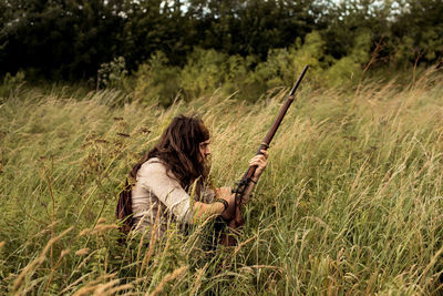 Man sitting on grass in field holding prop gun