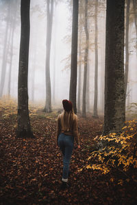 Full length of woman standing by tree in forest during autumn