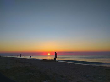 Silhouette woman standing at beach against sky during sunset