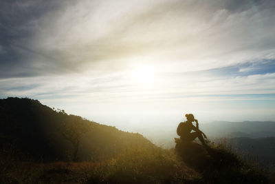 Silhouette man sitting on mountain against sky