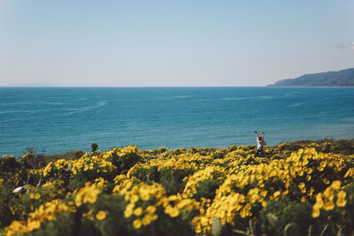 Distant view of mid adult woman jumping amidst yellow flowers against sea