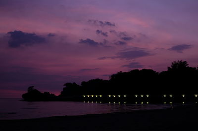 Silhouette trees on beach against romantic sky at sunset