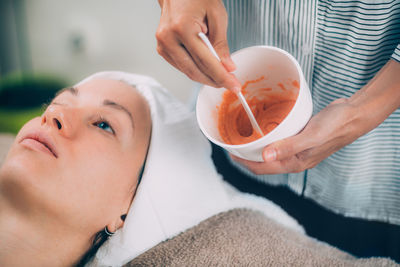 Midsection of beautician applying face mask on woman