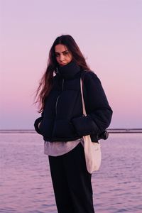 Portrait of smiling young woman standing against sea during sunset