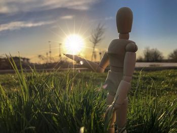 Close-up of wooden figurine on grassy field against sky during sunset