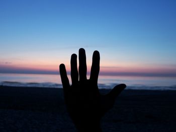 Close-up of silhouette hand against sea at sunset