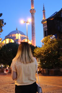 Rear view of woman with blond hair standing in city at dusk