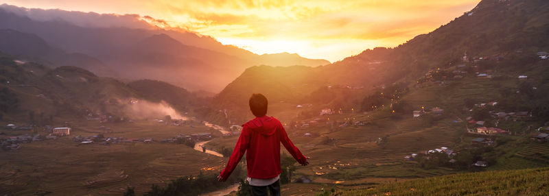 Rear view of man standing against mountain during sunset