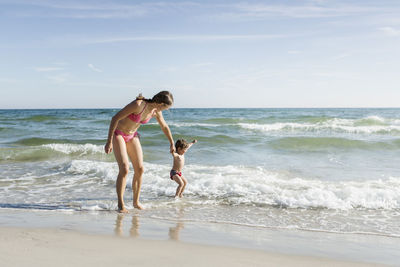 Mother with daughter enjoying on beach against sky during sunny day