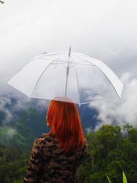 Rear view of woman standing on umbrella during rainy season