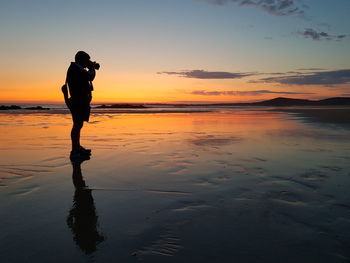 Man photographing sea against sky during sunset