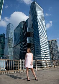 Full length of woman standing against modern buildings in city against sky