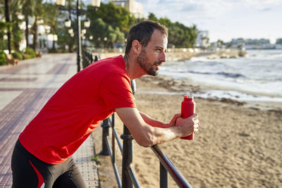 Smiling man holding water bottle leaning on railing