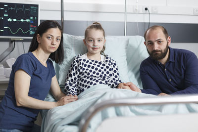 Parents with daughter sitting on bed in hospital ward