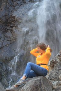 Woman sitting on rock by waterfall