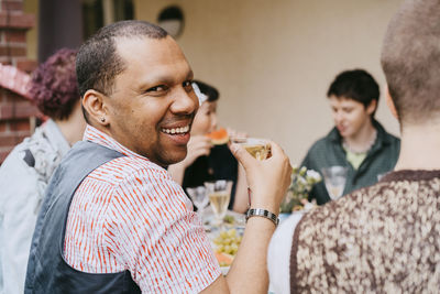 Portrait of smiling gay man having drink with friends during party in back yard