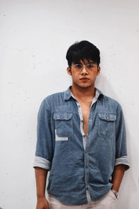 Portrait of serious young man standing against wall