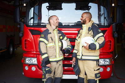 Happy firefighters talking while standing in front of fire engine at fire station