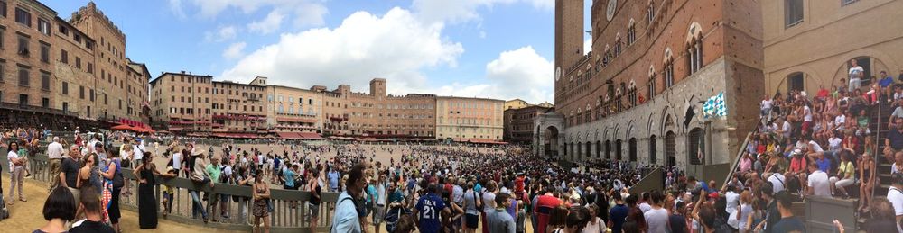 Panoramic view of people in town square against sky