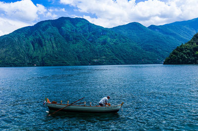 Man sailing on boat in lake against mountains