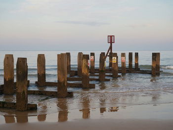 Wooden posts in sea against sky