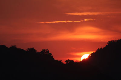 Silhouette trees against dramatic sky during sunset