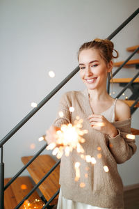 Smiling young woman holding sparkler at home