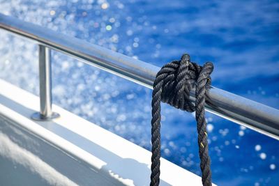 Close-up of rope tied on railing on a moving boat against background of sea spray and blue sea