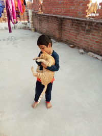 Full length of boy holding cat while standing at terrace 