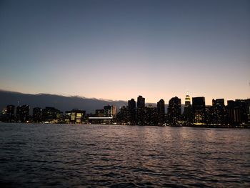 River by illuminated buildings against sky during sunset