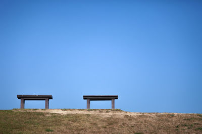 Empty bench on field against clear blue sky