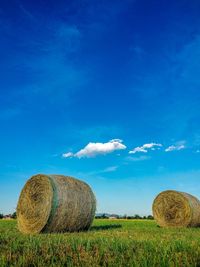 Hay bales on field against blue sky