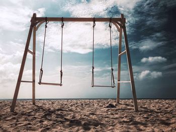 Empty swing on beach against sky