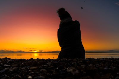 Silhouette man looking at sea against sky during sunset