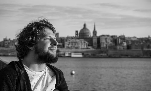 Young man looking away against river in city