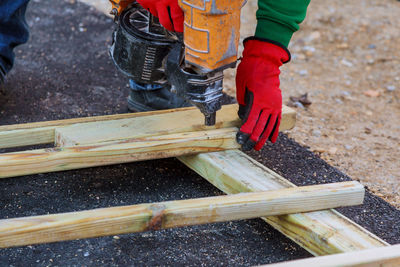 Low section of carpenter using nail gun on wood at construction site