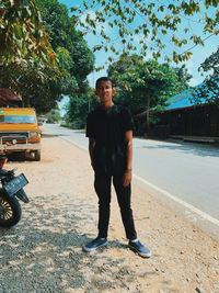 Young man standing on road against trees