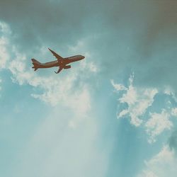 Low angle view of airplane flying against cloudy sky