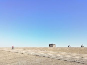 People walking on land against clear blue sky