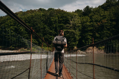 Man standing by railing in forest against sky