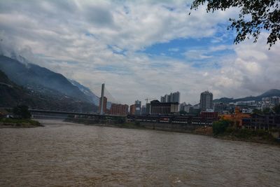 Bridge over river by buildings against sky in city