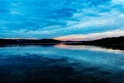 Scenic view of lake against cloudy sky at sunset