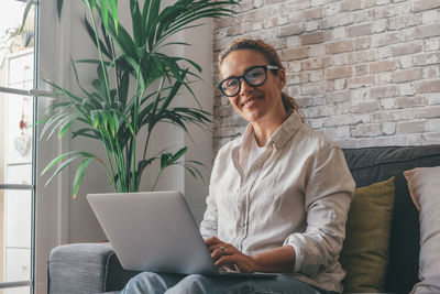 Young woman using laptop while sitting on sofa at home