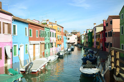 Boats moored in canal amidst buildings in city against sky