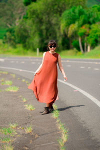 Young woman wearing sunglasses walking on road against trees in forest