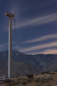 Low angle view of moving wind turbine against star trails on field