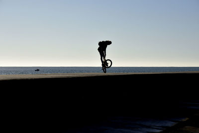 Silhouette man riding bicycle on sea against clear sky