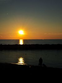 Silhouette people on beach against sky during sunset