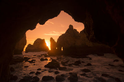 Rock formations on shore seen through cave during sunset