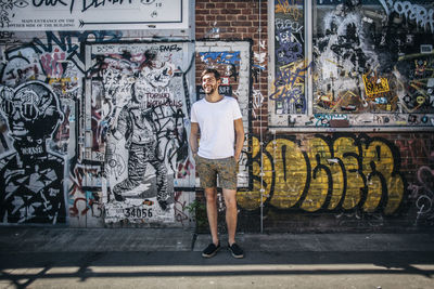 Full length portrait of smiling standing against graffiti wall